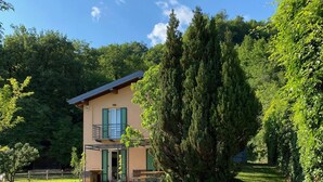 A house with a stone pathway leading to the entrance, surrounded by lush greenery and large trees. - LA COMMISSERIA Beautiful new house with private pool surrounded by nature (Salò)