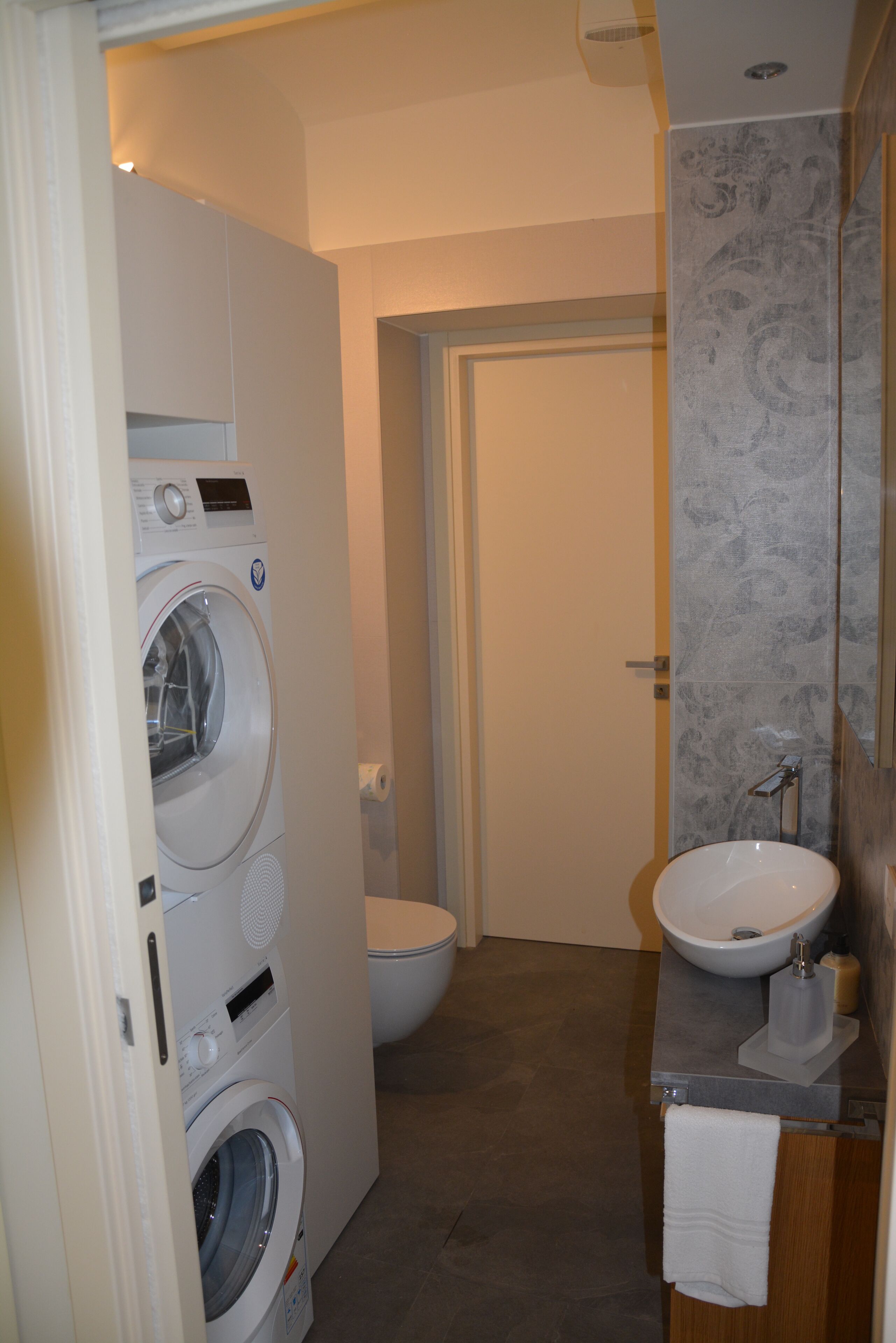 Une petite salle de bain équipée d’un lave-linge, de toilettes et d’un lavabo.