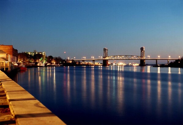 A nighttime view of a river with a bridge and buildings along the riverbank. - Water Street Retreat 14 (Wilmington)