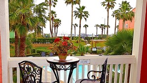 Un balcon avec une table et deux chaises, donnant sur une piscine et des palmiers.