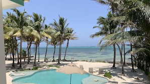 A pool area with lounge chairs and umbrellas, surrounded by palm trees and a view of the ocean. - Coral Bay Villas (San Pedro)