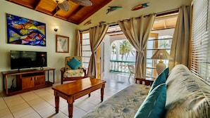 A living room with a wooden ceiling, a television on a cabinet, a sofa with a tropical print, and a painting of fish on the wall. - Coral Bay Villas (San Pedro)