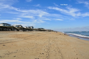 A beach with footprints, a pier, and houses in the background.