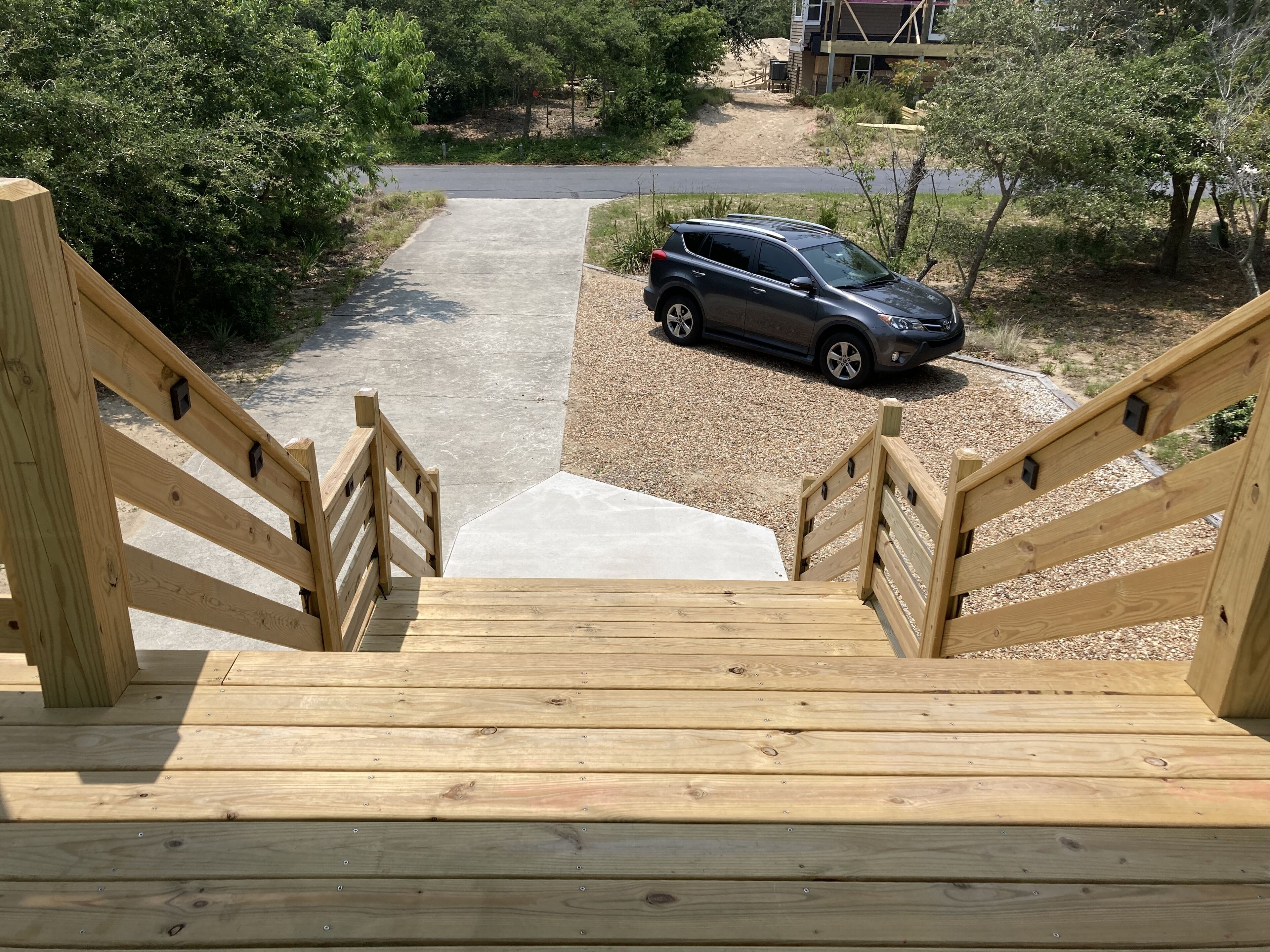 A wooden staircase leading to a driveway with a parked car.