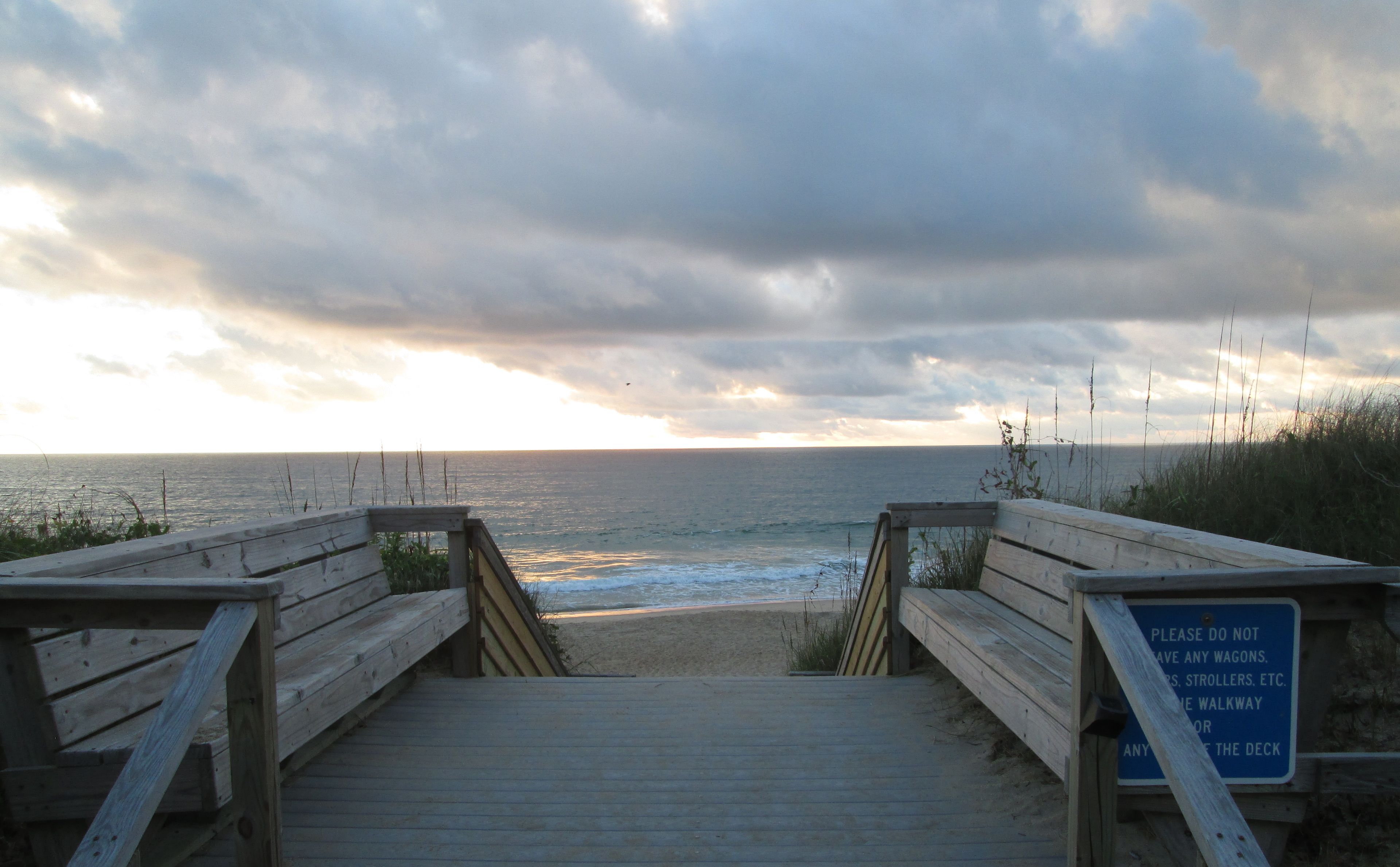 A wooden boardwalk leading to a beach with a sign prohibiting the use of wagons, strollers, etc.