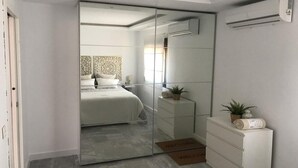 Ein modernes Schlafzimmer mit einem großen Spiegel, einem Bett, einer Kommode und einer kleinen Pflanze.
