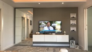 Ein modernes Wohnzimmer mit einem flachbildfernseher an einem weißen Schrank, einer Glastür zu einem weiteren Raum und gerahmten Stadtbildern an der Wand.