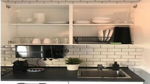 A kitchen with white cabinets, a black countertop, a stainless steel sink, a microwave, and a potted plant.