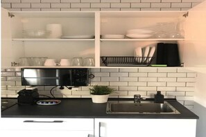Een keuken met witte kastjes, een zwart aanrecht, een roestvrijstalen spoelbak en een magnetron, en een kamerplant.
