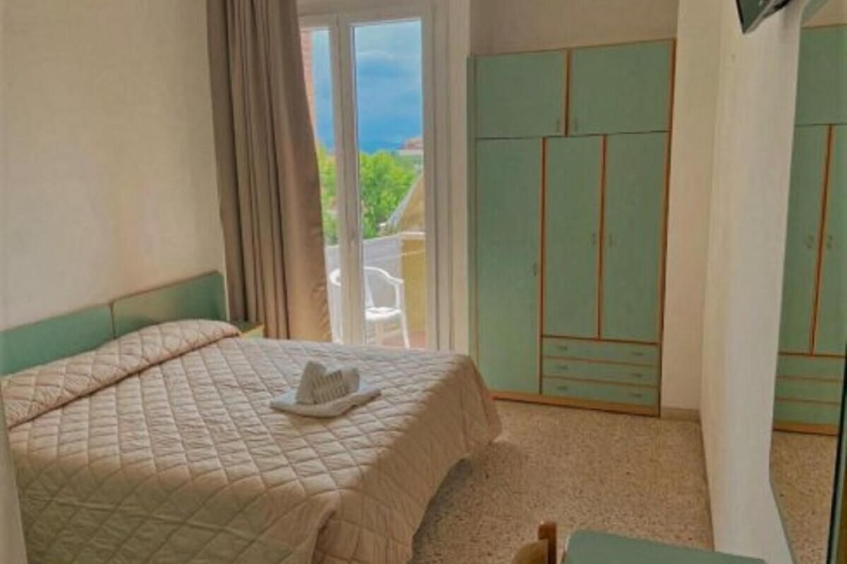 A bedroom with a bed, a desk, a wardrobe, and a view of the outdoors.