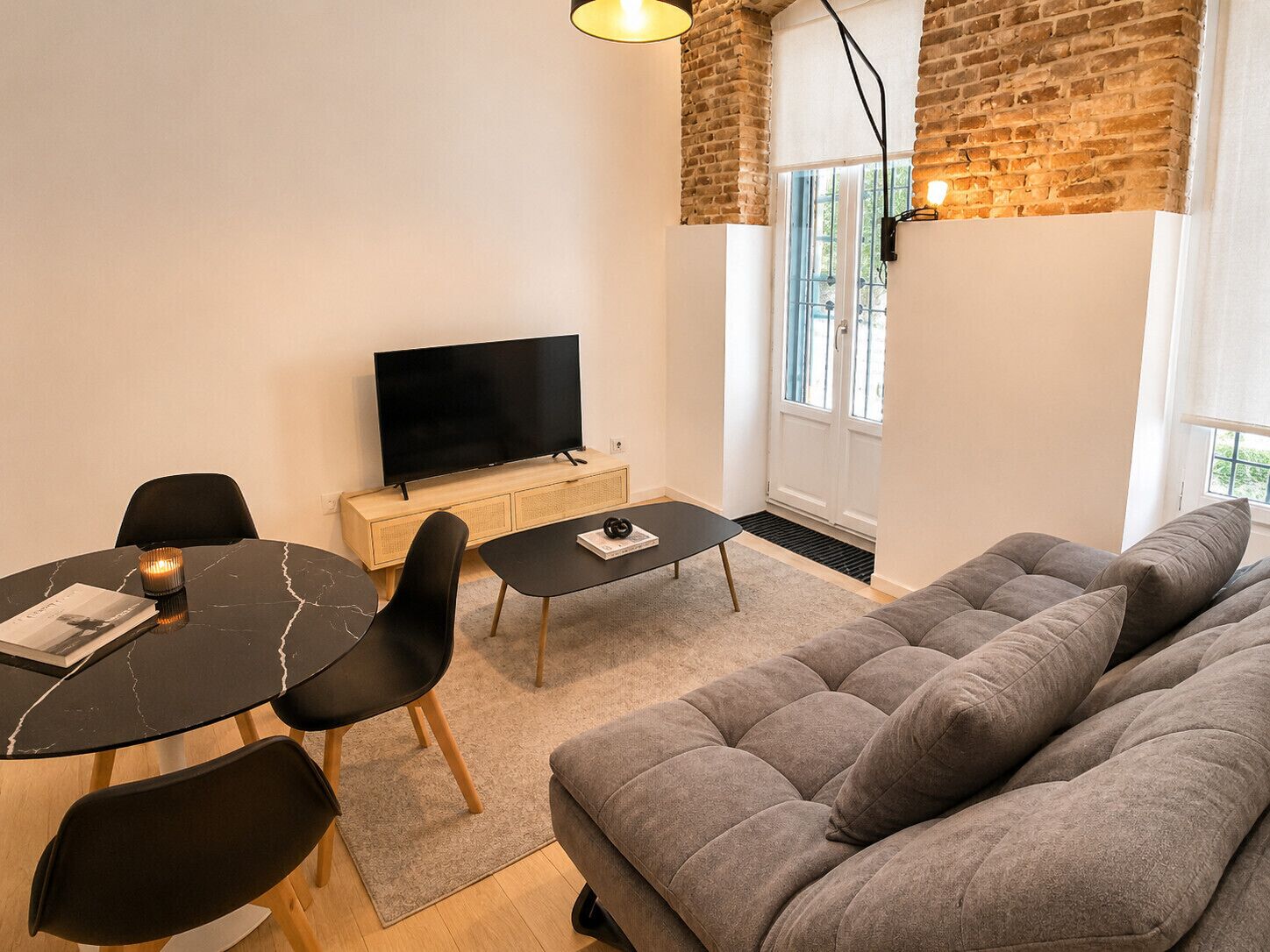 Una sala de estar moderna con un sofá, una mesa de comedor con sillas, un televisor de pantalla plana y una pared de ladrillo.