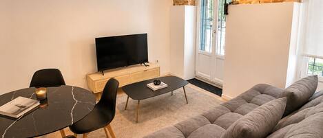 Una sala de estar moderna con un sofá, una mesa de comedor con sillas, un televisor de pantalla plana y una pared de ladrillo.