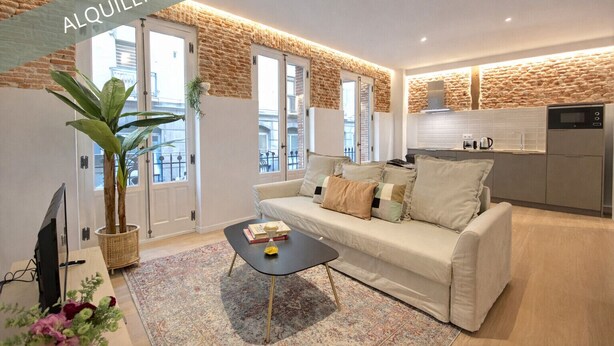 Un appartement moderne avec un mur d’accent en pierre, un canapé, une table basse et un coin cuisine.