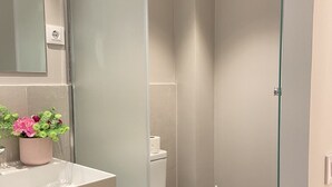 Une salle de bain moderne avec une douche à parois de verre, des toilettes blanches et un lavabo agrémenté d’un vase de fleurs.