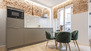 Una cocina moderna con salpicadero de pared de piedra, horno empotrado y comedor con sillas verdes.