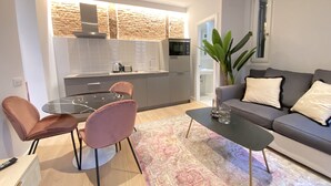 Ein modernes Wohnzimmer mit einem grauen Sofa, rosafarbenen Sesseln, einem Glastisch und einem gemusterten Teppich.