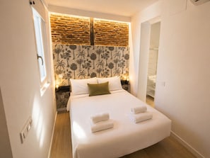 Un dormitorio con una cama, una mesita de noche, una pared con diseño de ladrillo y una puerta que da a un armario.