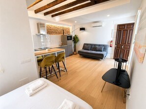 Um espaço compacto com cozinha compacta, sofá, área de refeições com cadeiras e TV.