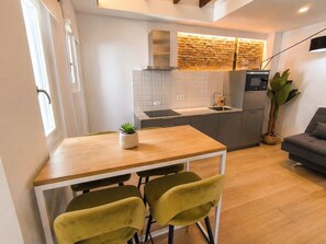 Uma cozinha compacta com área de refeições, um sofá cinzento e um vaso com planta.