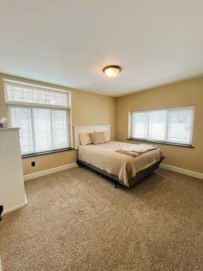 A bedroom with a bed, two windows with blinds, a ceiling light, and beige walls. - Lake House Villa by HHSW (Logan)