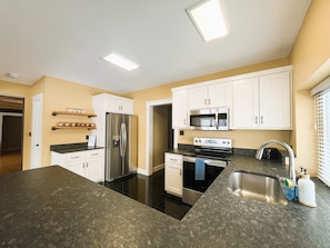 A modern kitchen with white cabinets, stainless steel appliances, and granite countertops.