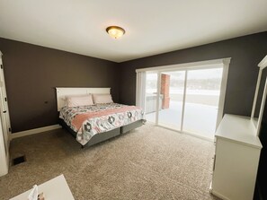 A bedroom with a bed, a carpeted floor, a white dresser, and a sliding glass door leading to a balcony.