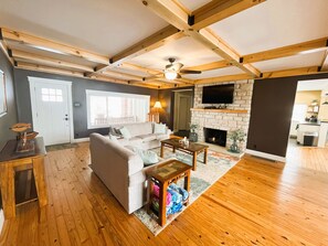 A spacious living room with a fireplace, wooden beams, a sofa, and a television.