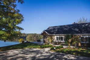 A lakeside cabin with a covered patio, a barbecue grill, and a view of the lake.