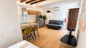 Un espace de vie compact comprenant un coin cuisine, un canapé, un coin repas avec des chaises et un téléviseur.