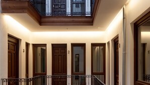 Un couloir avec des portes en bois numérotées de 2 à 5, un balcon doté d’une balustrade en fer forgé et un escalier menant à l’étage supérieur.