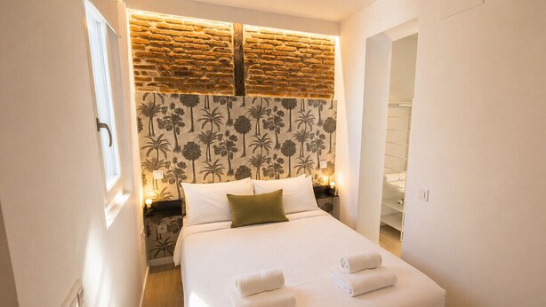 Une chambre à coucher comprenant un lit, une table de chevet, un mur avec un motif en briques et une porte donnant sur un placard.