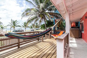 A wooden deck with a hammock, palm trees, and a view of the ocean. - Casita Playa del Parque (San Pedro)