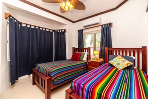 A room with two wooden beds, dark curtains, a ceiling fan, and a window with curtains. - Casita Playa del Parque (San Pedro)