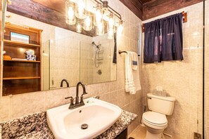 A bathroom with a white sink, a mirror, a shower, and a toilet.