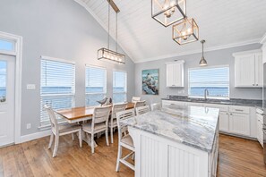 A kitchen with white cabinetry, a marble island, and a view of the ocean through large windows.