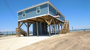 Una casa a due piani con un patio in legno, una scala e vista sulla spiaggia.
