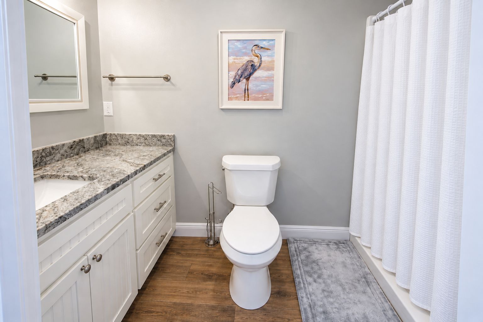 A bathroom with a toilet, a marble countertop, a framed painting, and a shower curtain.
