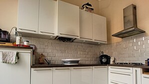 Een keuken met witte kasten, een tegelwand van baksteen, een gasfornuis en een koffiezetapparaat.