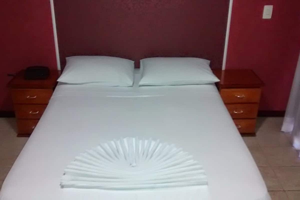 A neatly made bed with a white bedspread and pillows, flanked by wooden nightstands with drawers, in a room with red walls and a tiled floor.