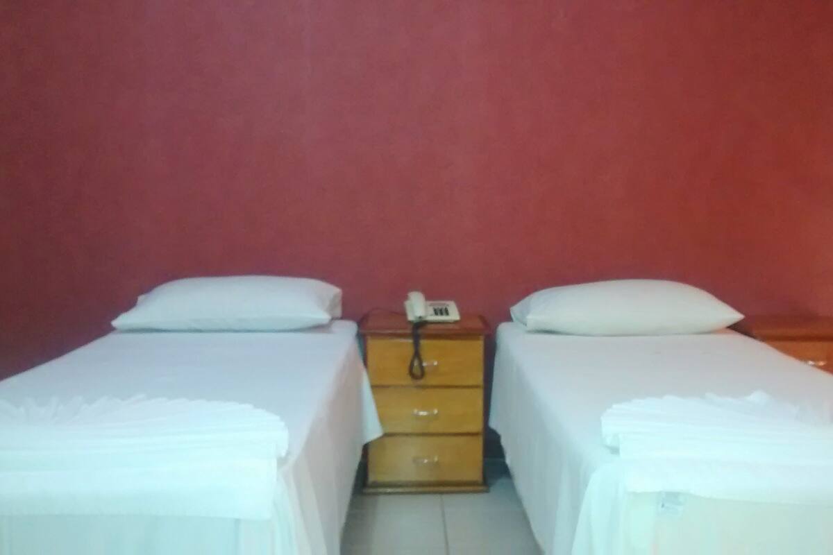 A small room with two single beds, a wooden nightstand with a telephone, and a red wall.