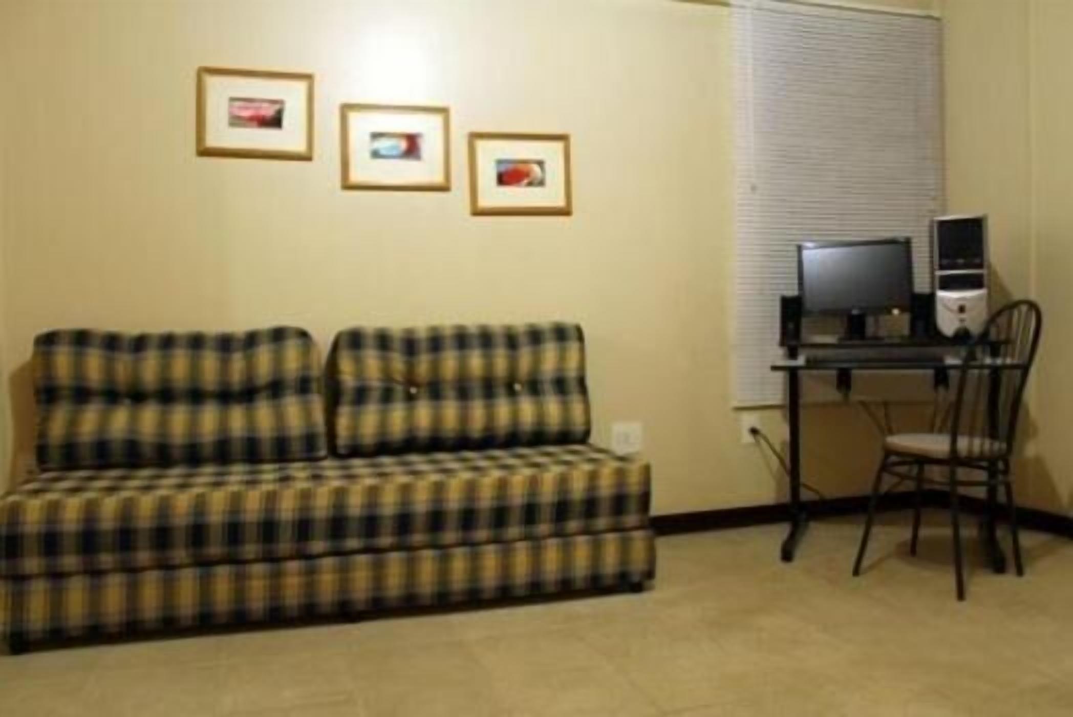 Quarto com sofá xadrez, escrivaninha com computador e uma cadeira.