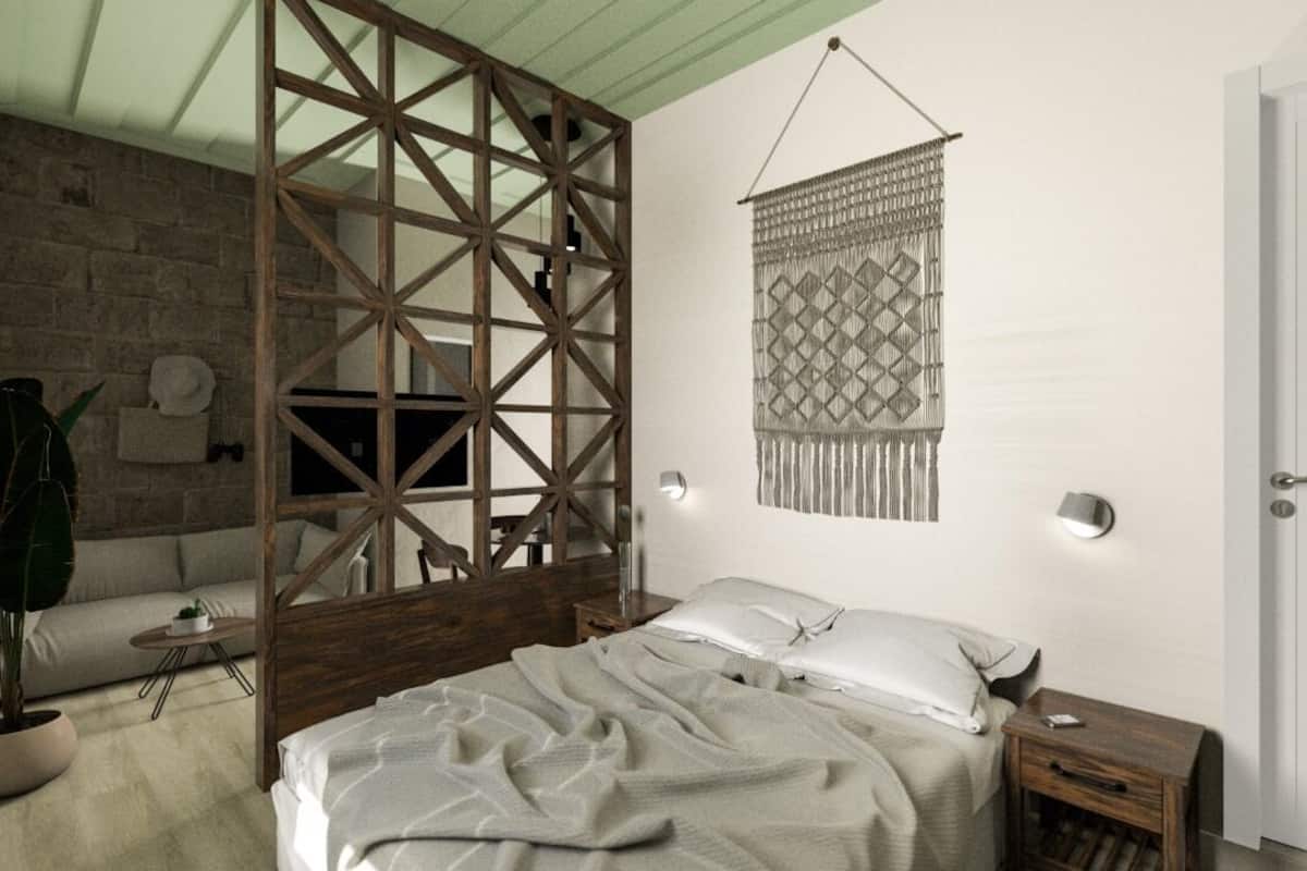 A bedroom with a bed, a wooden partition, a hanging textile, a bedside table, and a potted plant.