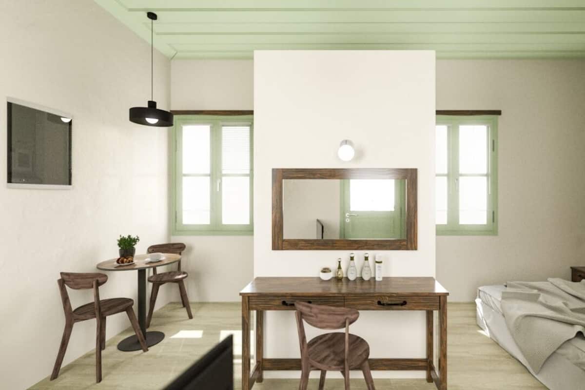 A room with a wooden desk, two chairs, a mirror, and a bed.