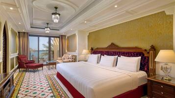 A spacious hotel room with a large bed, a sitting area with a chair and a small table, a balcony with a view, and a decorative carpet.