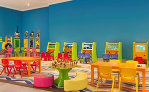 A brightly colored children's play area with tables, chairs, and educational screens.