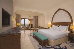 A hotel room with a large bed, a desk, a bench, a sofa, a TV, and a balcony with a view. - Doubletree by Hilton Resort & Spa Marjan Island (Ras Al Khaimah)