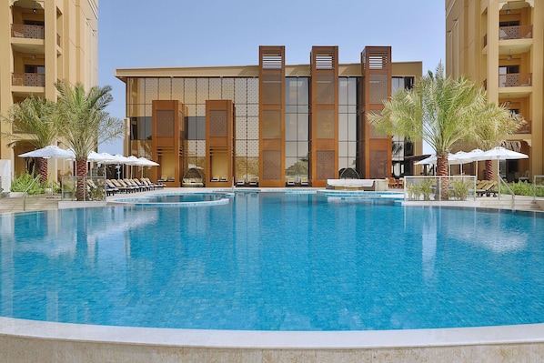 A hotel with a large pool, sun loungers, and palm trees. - Doubletree by Hilton Resort & Spa Marjan Island (Ras Al Khaimah)