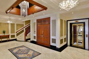 A grand lobby with a marble floor, a large wooden door, a staircase, and a chandelier.