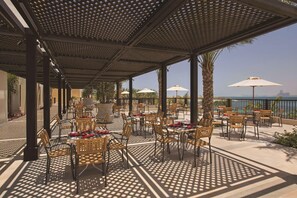 An outdoor patio with tables and chairs, umbrellas, and a view of the sea.