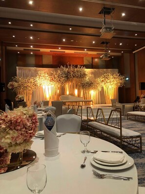 A banquet hall with round tables, white tablecloths, and floral centerpieces.